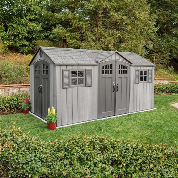 Gray storage shed with double doors, a single door, window shutters, and shingled roof sits on a lawn.