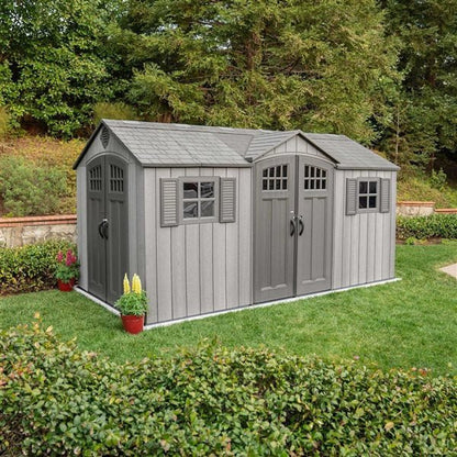 Gray storage shed with double doors, a single door, window shutters, and shingled roof sits on a lawn.