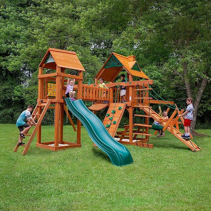 Children play on a wooden backyard playset with a slide, climbing wall, ladders, and rope bridge.