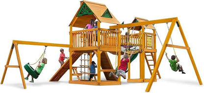 Children play on a wooden playground with swings, a slide, a climbing net, and a playhouse.