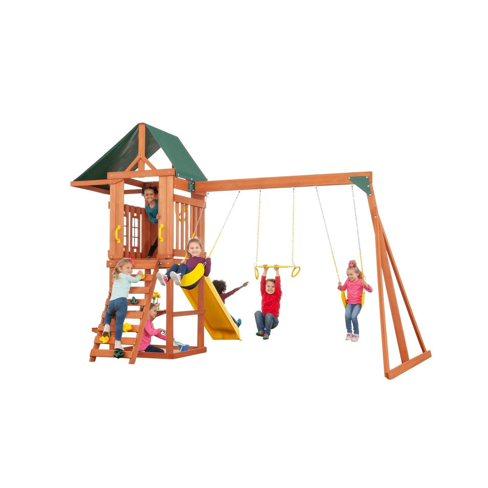 Five children play on the Creative Cedar Designs Cedar Cottage Wooden Swing Set, which features a wooden slide, swings, climbing wall, and playhouse, all set against a white background.
