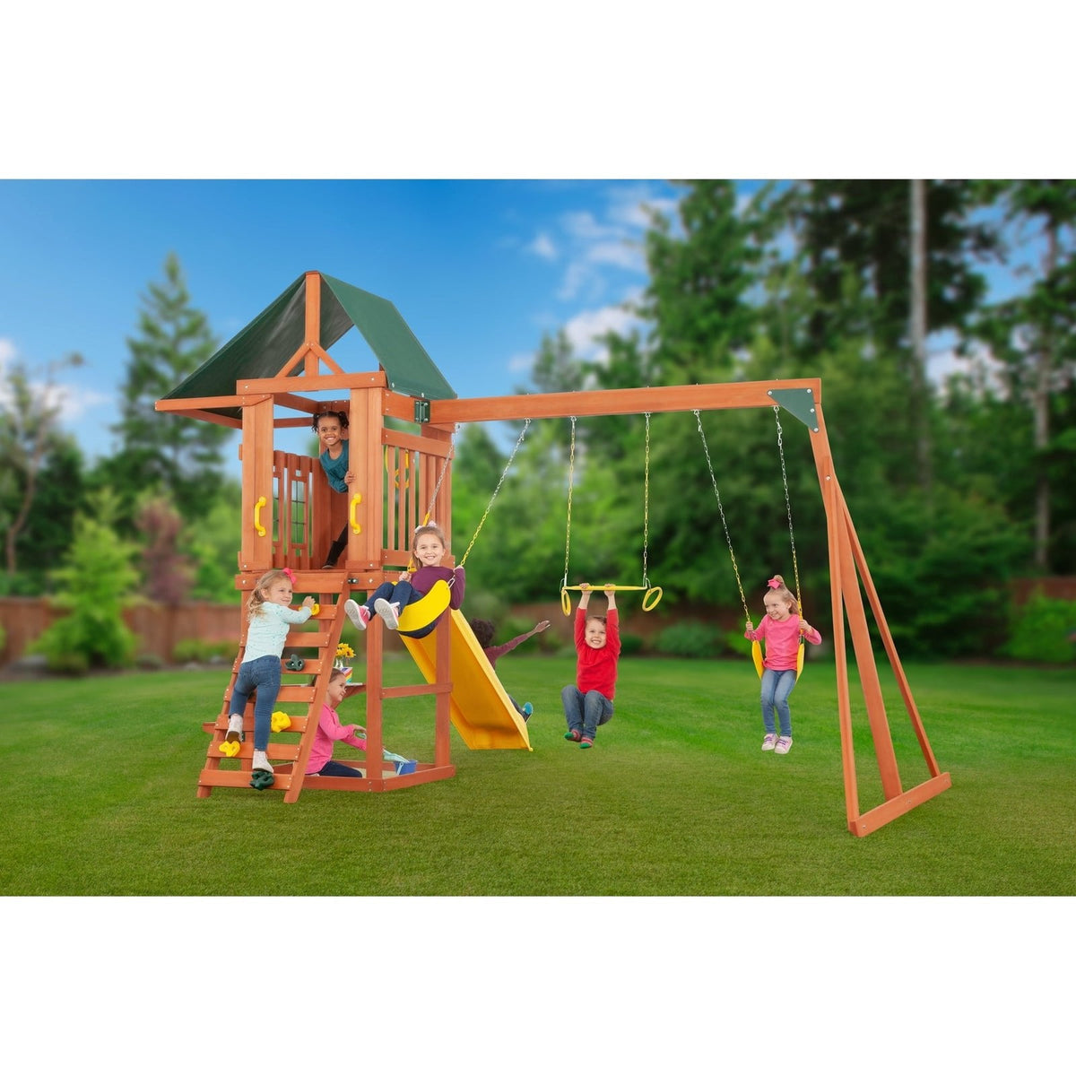 Children play on a wooden swing set with a slide, climbing wall, and swings under a blue sky.